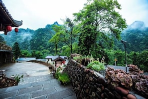 A traditional courtyard with stone walls, a wooden fence, and a view of a mountainous landscape.