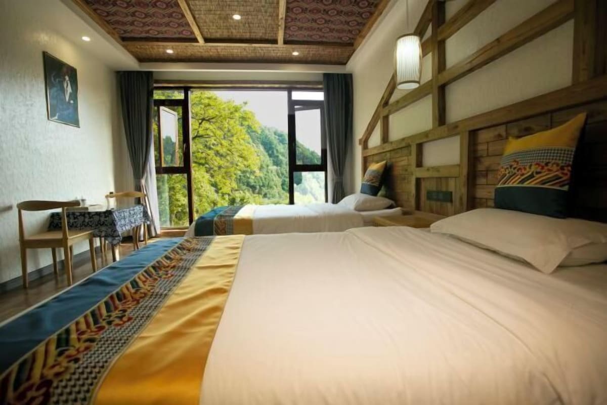 A hotel room with two beds, a view of greenery outside, and a traditional ceiling design.