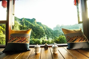 A room with a wooden floor, two patterned pillows, and a small table with two ceramic jars and a vase with a single flower.