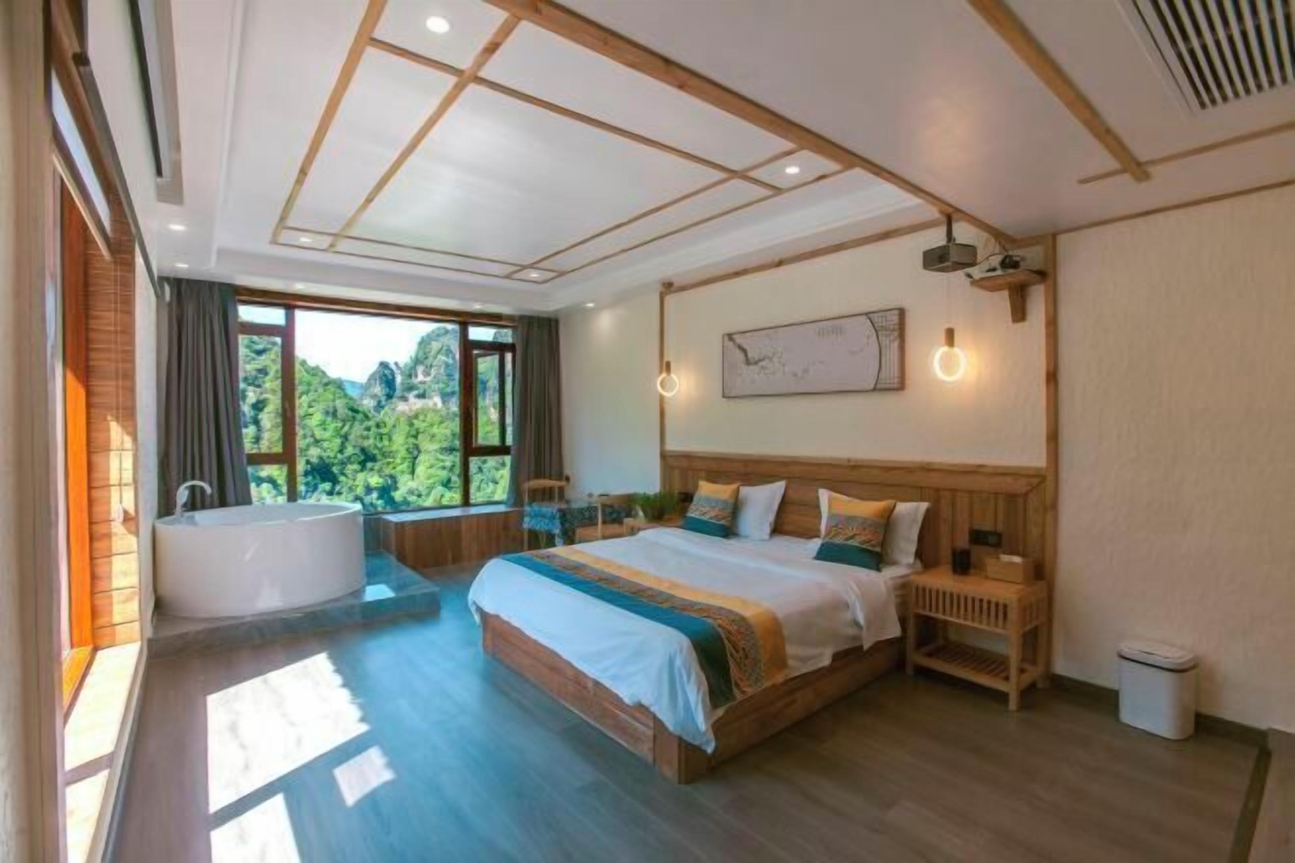 A spacious bedroom with a large bed, a bathtub, and a view of greenery.