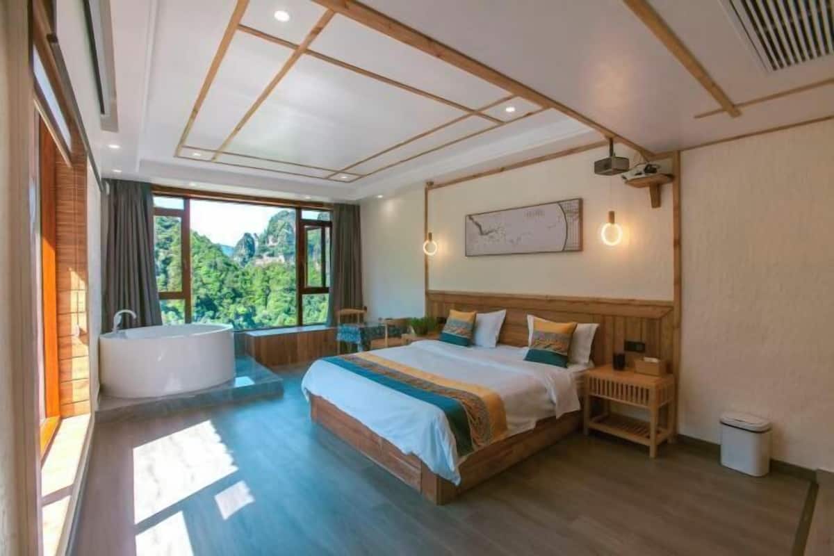 A spacious bedroom with a large bed, a bathtub, and a view of greenery.