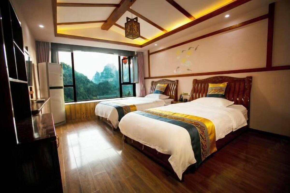 Habitación de hotel con dos camas, suelo de madera, un ventanal con vistas y techo de vigas de madera con iluminación empotrada.
