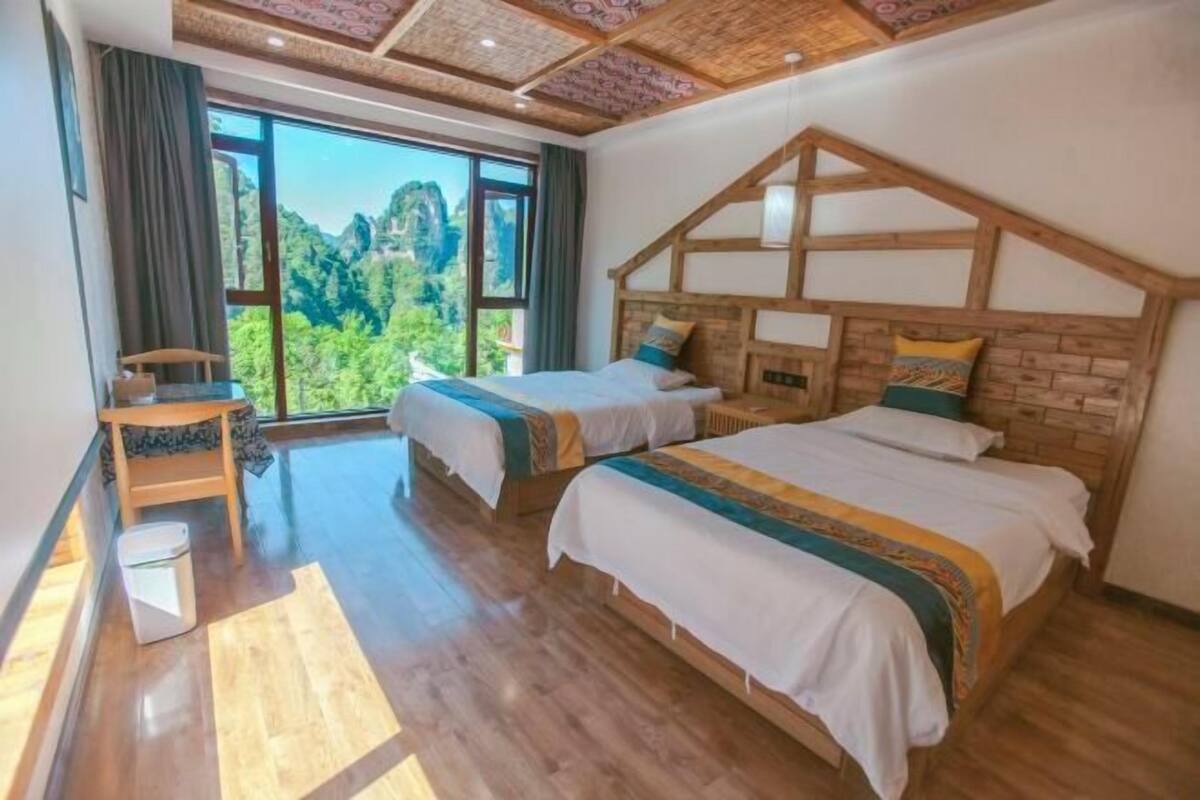 Habitación de hotel con dos camas, techo de madera y un ventanal con vistas a la montaña.