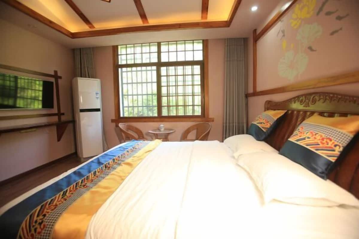 A hotel room with a bed, a small table, a refrigerator, and a window with bars.