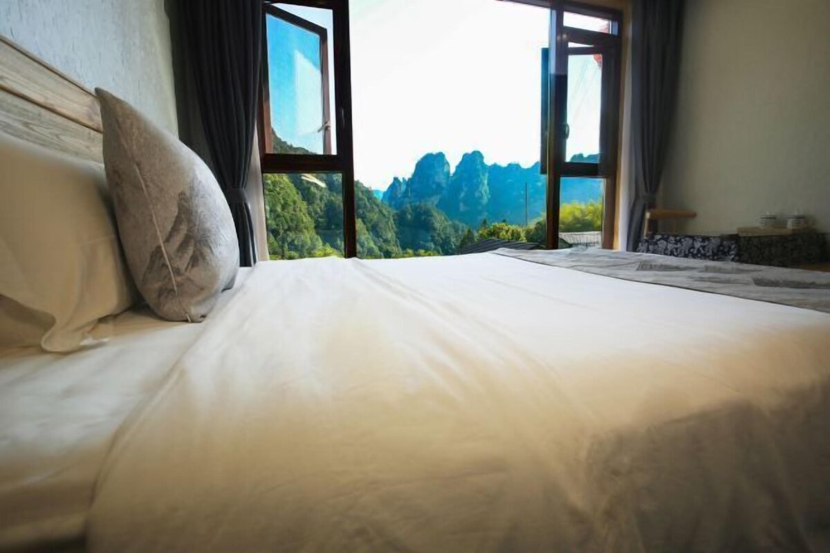 A bed with a view of a mountainous landscape through large windows.