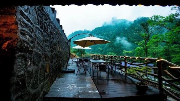 An outdoor dining area with stone walls, tables, and umbrellas, overlooking a forested valley. - Zhangjiajie Xianlv Residential Accommodation (Wulingyuan National Scenic Spot Scenic Spot Store) (Zhangjiajie)