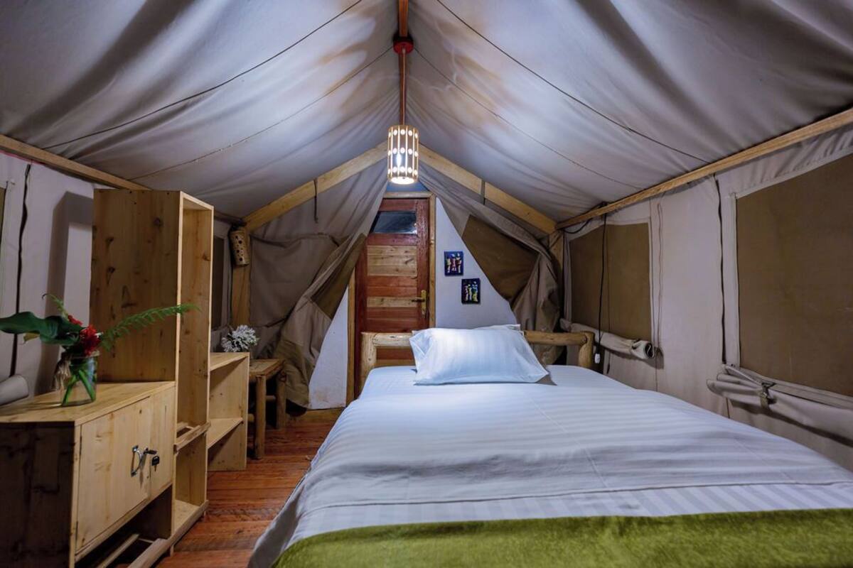 Una habitación con tienda de campaña, una cama, muebles de madera y una lámpara colgante.