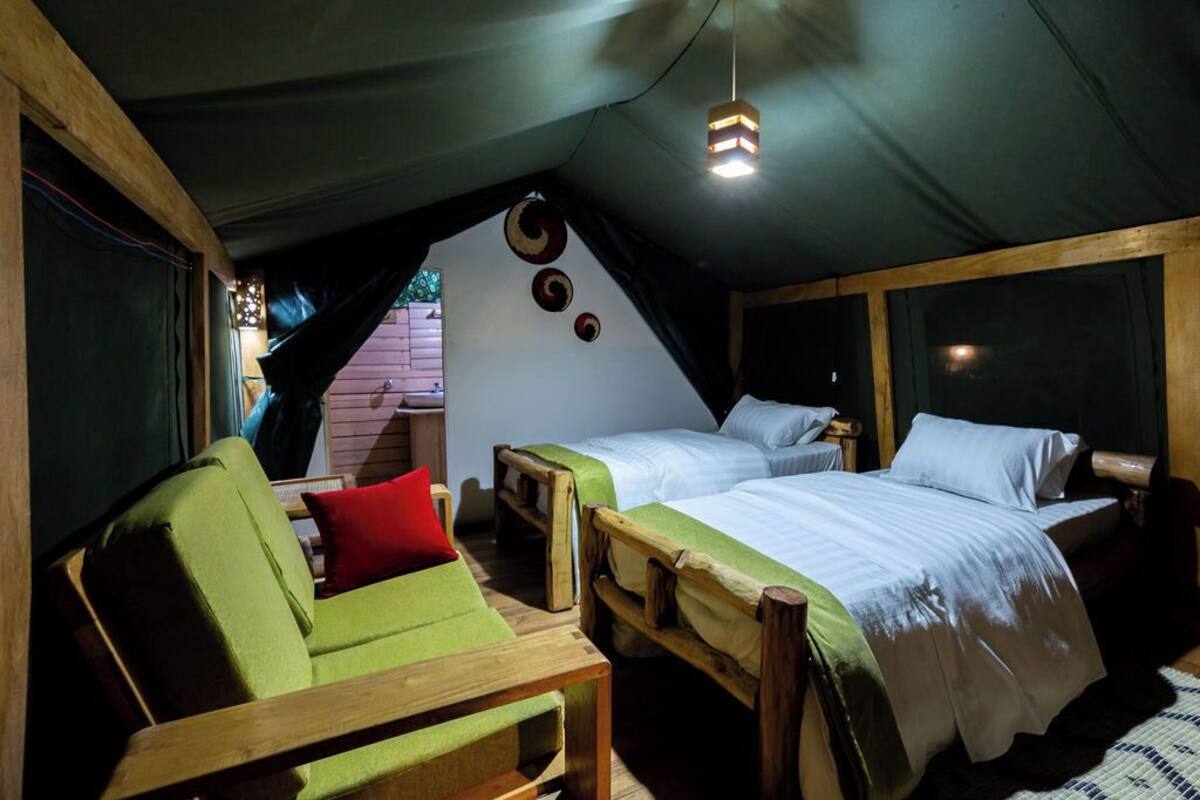 Un dormitorio cálido en el ático con dos camas de madera, una silla verde y una mesita pequeña.