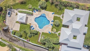 An aerial view of a residential area with a swimming pool, stone patio, and a small garden.