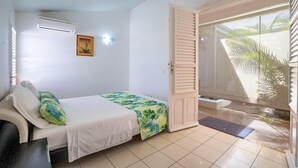A bedroom with a bed, a door leading to a balcony, a wall-mounted air conditioner, and a framed picture.