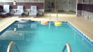 An indoor swimming pool with clear water, a diving board, and lounge chairs. - La VOD Hotel (Benin City)