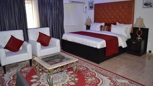 A hotel room with a large bed, two white armchairs, a small coffee table, and a red patterned rug. - La VOD Hotel (Benin City)