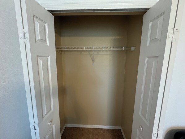 A walk-in closet with a beige wall, white doors, and a metal rod for hanging clothes.