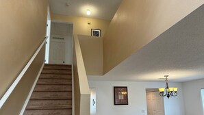 Ein mehrgeschossiges Interieur mit Teppichstufen, einem Kronleuchter, einem bequemen Ohrensessel und einem gerahmten Kunstwerk an der Wand.