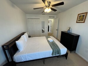 Een slaapkamer met een bed, een plafondventilator, een dressoir en een deur naar een andere kamer.