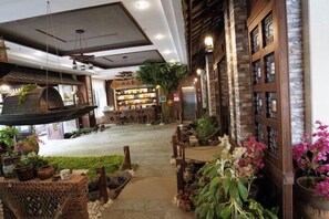 Relax in a cozy space with a high ceiling, wooden bench, and hanging chair, surrounded by natural touches and warm lighting.
