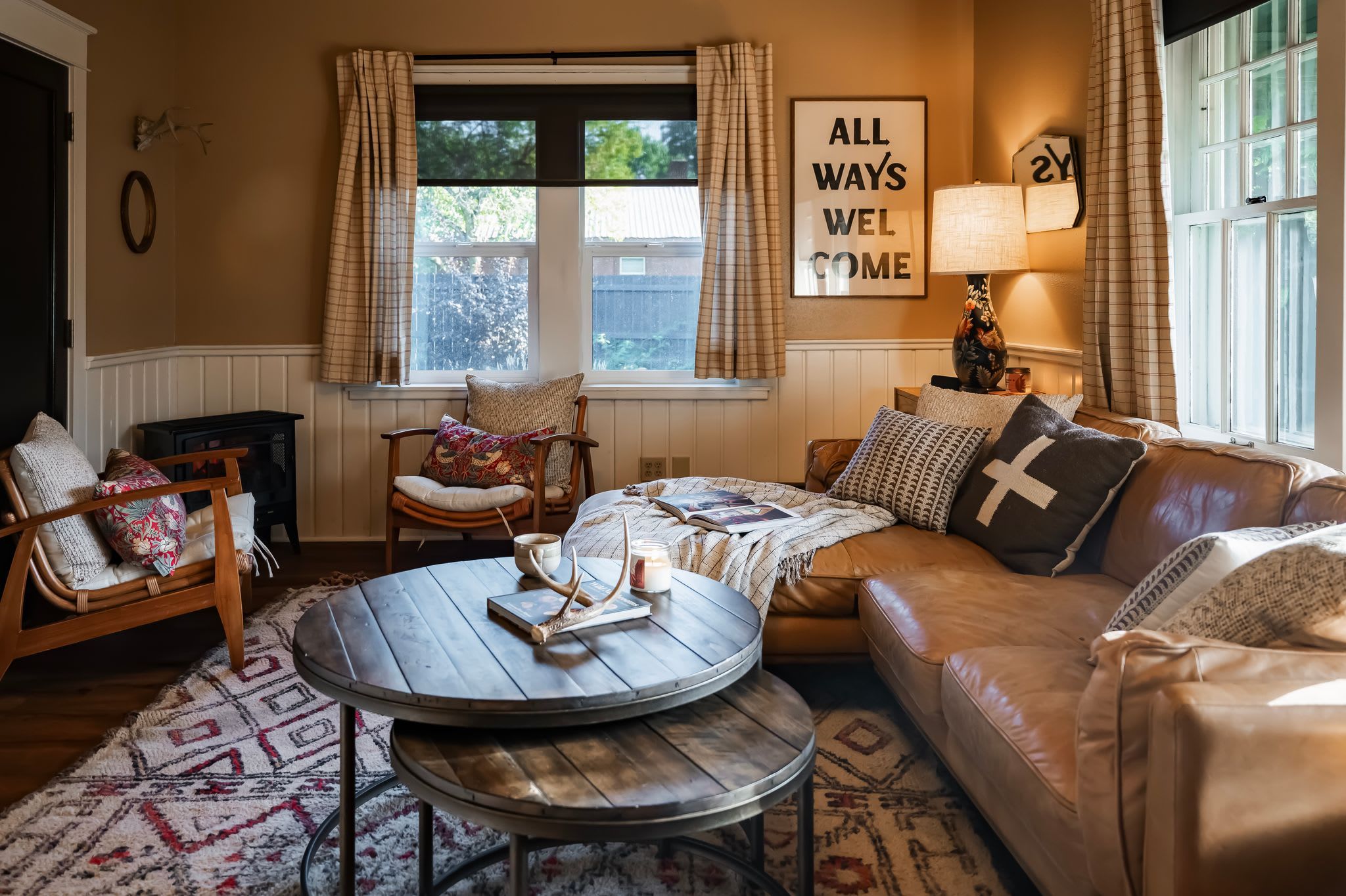 A cozy living room with a leather sofa, a round wooden coffee table, a wicker chair, and a patterned rug.
