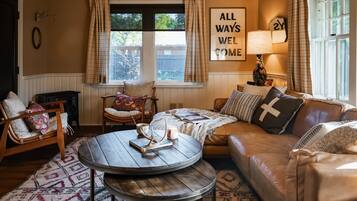A cozy living room with a leather sofa, a round wooden coffee table, a wicker chair, and a patterned rug.