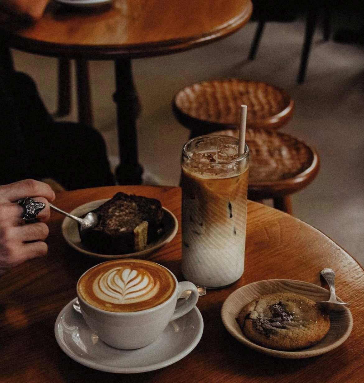 A table with a cup of coffee, a glass of iced coffee, a plate with a cookie, and a plate with a dessert.
