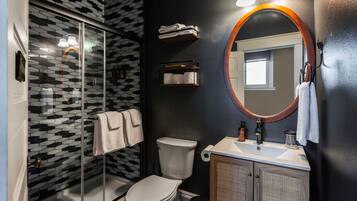 A modern bathroom with a glass shower enclosure, a toilet, a sink with a mirror, and a towel rack.