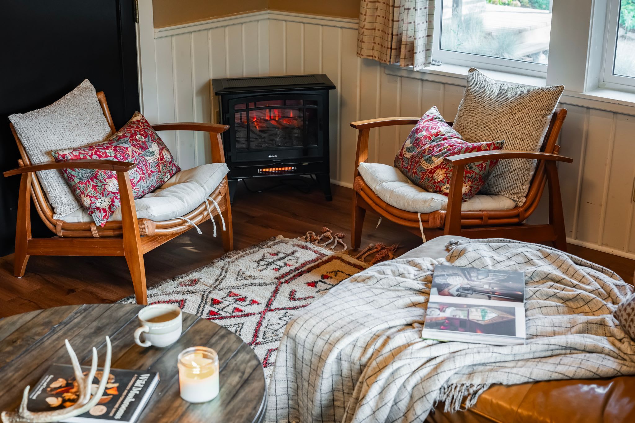 A cozy room with two wicker chairs, a small table with a cup and a candle, and a blanket on a bed.
