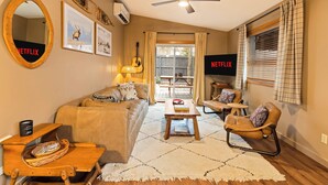 Een gezellige woonkamer met een bank, salontafel en fauteuils, een plafondventilator en een televisiescherm waarop 'NETFLIX' staat.