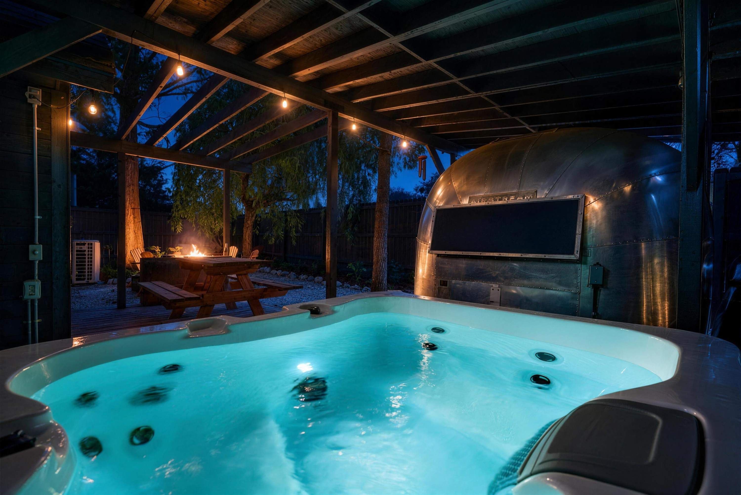 A hot tub with a wooden deck and a barbecue grill in the background.