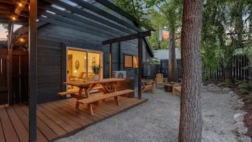 Enjoy outdoor dining on the covered patio with a wooden table and benches, surrounded by a serene natural landscape.