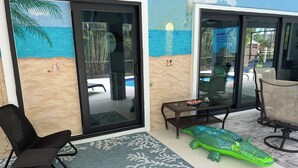 Ein Zimmer mit Glastür, die zu einem Poolbereich führt, einer grünen Alligator-Dekoration und einem kleinen Tisch mit Schlüsseln und einer Muschel.