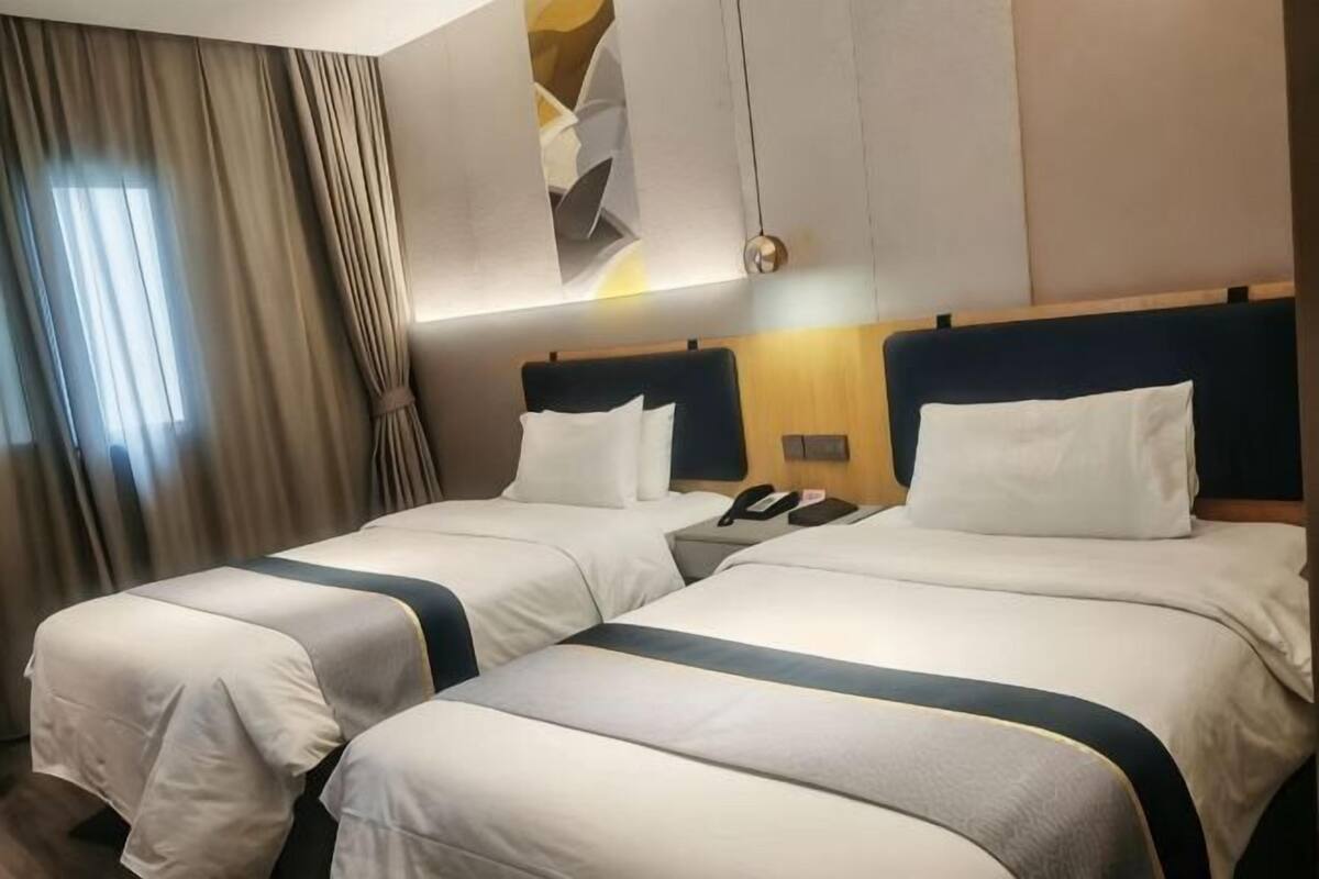 A hotel room with two beds, a nightstand, a telephone, and a window with curtains.
