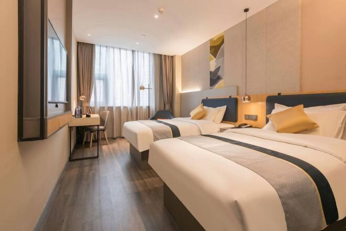 A hotel room with two beds, a desk, and a large window.