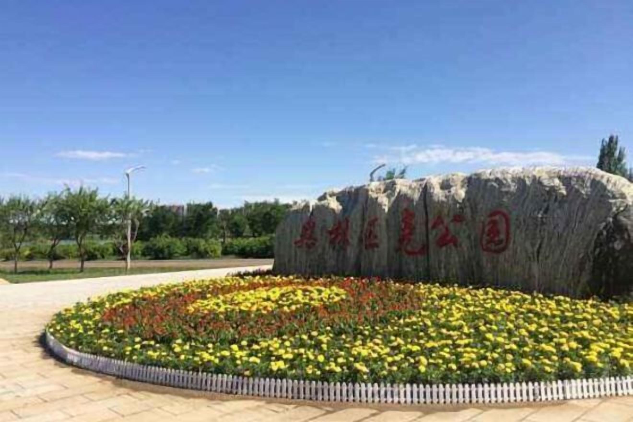 A large rock with inscriptions, surrounded by a circular flower bed with yellow and red flowers, and a white picket fence.