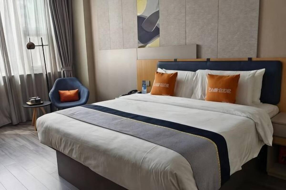 A hotel room with a large bed, a chair, a bedside table, and a wall-mounted artwork.