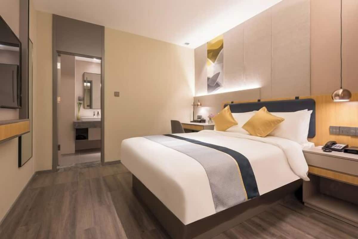 A hotel room with a bed, bedside table, and a mirror.
