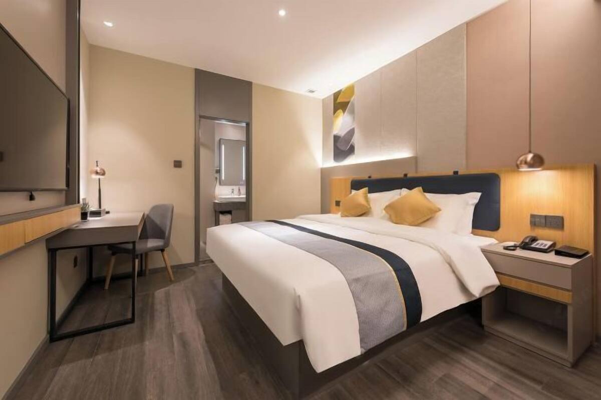 A modern hotel room with a large bed, bedside tables, a desk, and a chair.