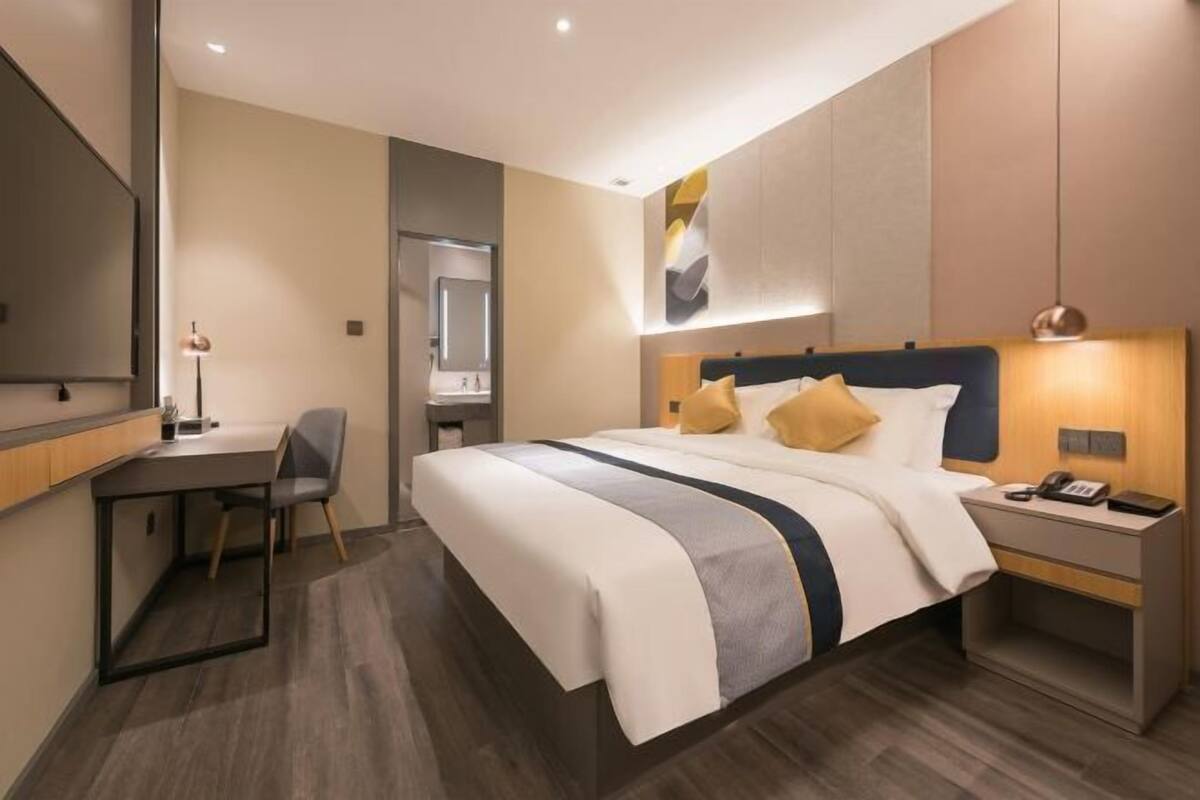 A modern hotel room with a large bed, bedside tables, a desk, and a mirror.