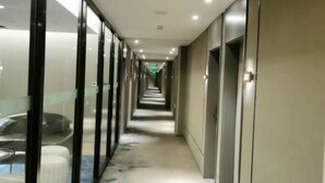 Un long couloir étroit, typique d’un hôtel, avec une paroi en verre d’un côté et un sol recouvert de moquette.