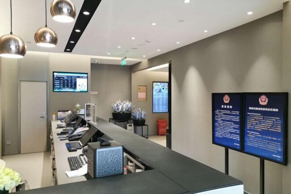Una zona de recepción con una larga barra de mostrador, varias estaciones de trabajo con computadoras y dos pantallas digitales grandes.
