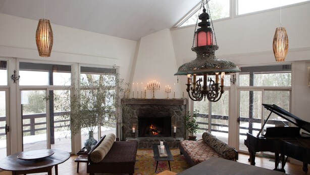 A spacious living room with a stone fireplace, a grand piano, and a large window overlooking a deck. - The Race Mountain House (Sheffield)