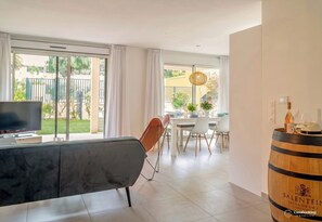 A modern living room with a flat-screen TV, a dining area with a table set for two, and a large window with curtains.