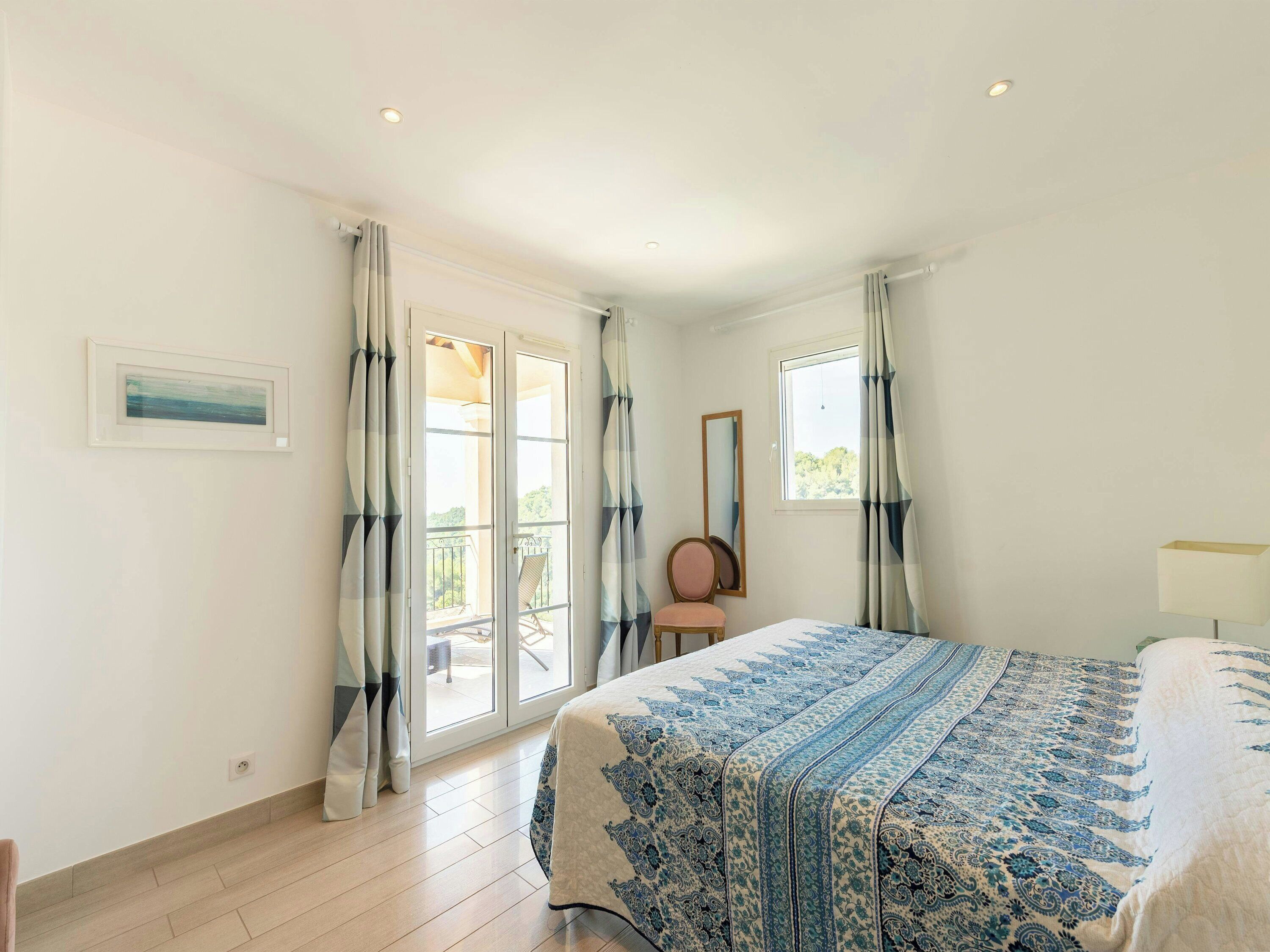 A bedroom with a bed, a chair, a window, and a door leading to a balcony.