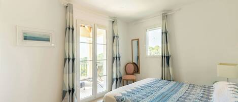 A bedroom with a bed, a chair, a window, and a door leading to a balcony.