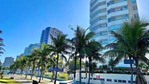 Un edificio moderno e slanciato con facciata in vetro, circondato da palme e un cielo azzurro intenso.
