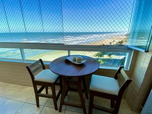 A balcony with a table and chairs, overlooking a beach and ocean. - Edifício Breno Navarro  (Praia Grande)