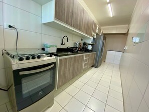 A kitchen with a stove, sink, and refrigerator, wooden cabinets, and tiled flooring. - Edifício Breno Navarro  (Praia Grande)