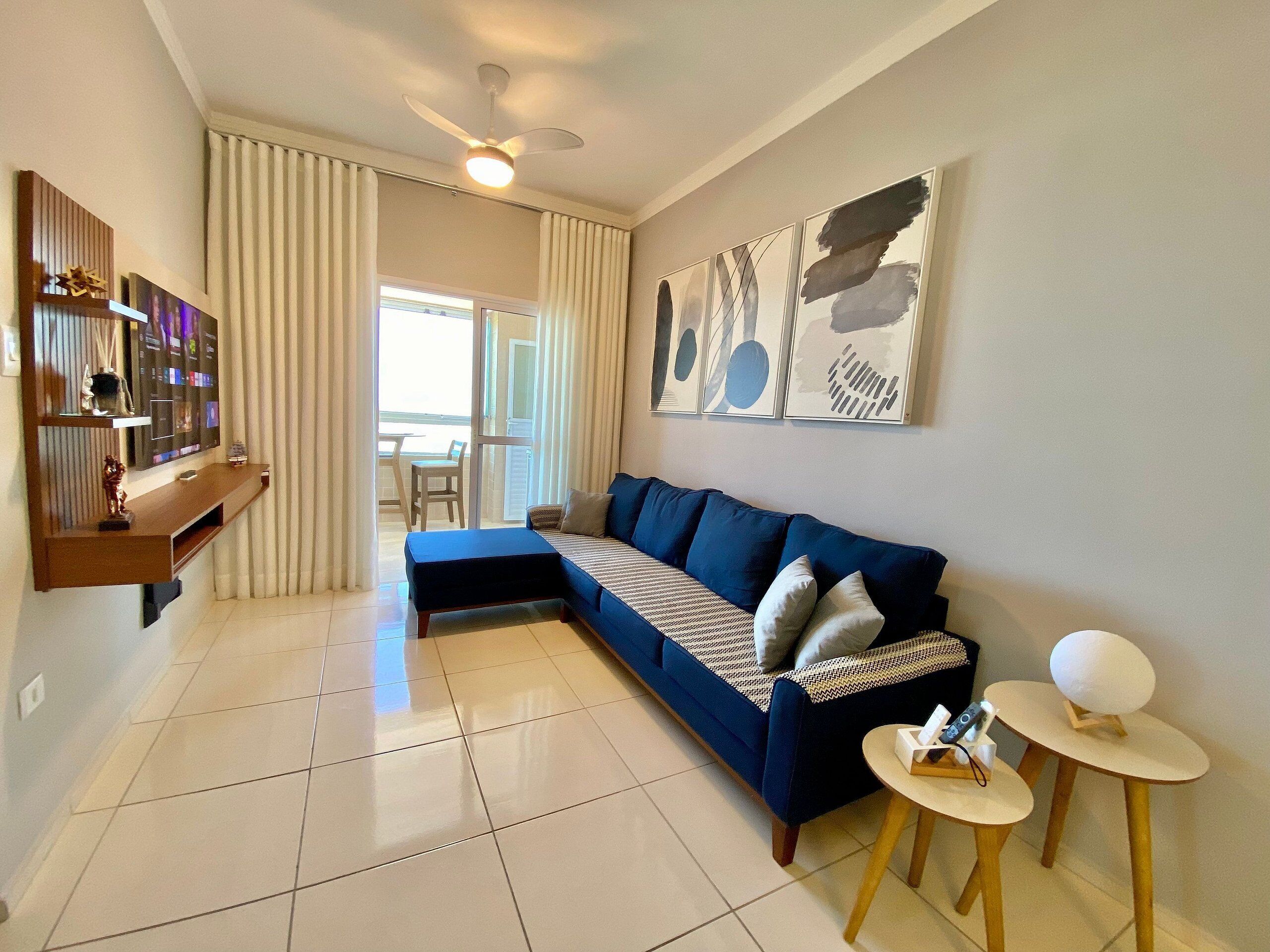 Una sala de estar con un sofá modular, un televisor sobre un mueble de madera, un ventilador de techo y obras de arte en la pared.