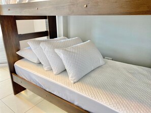 A bunk bed with white bedding and pillows, wooden headboard, and a light-colored wall. - Edifício Breno Navarro  (Praia Grande)