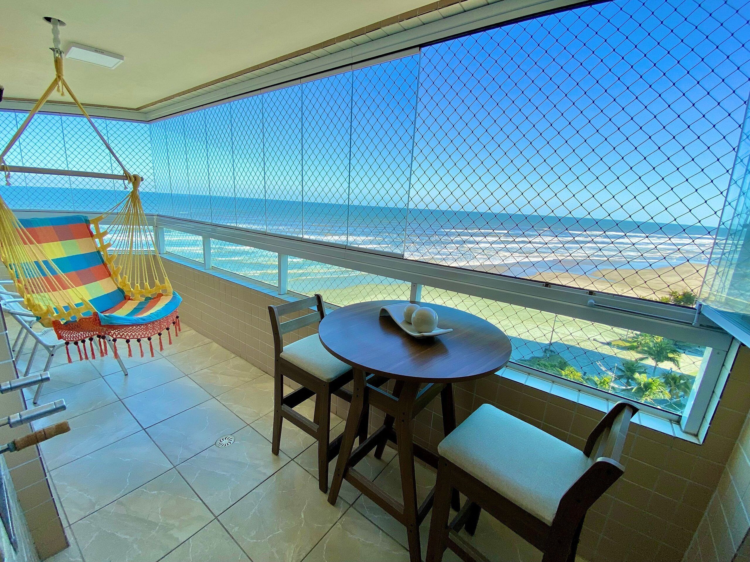 Un balcón con vista a la playa, una hamaca, una mesa con un plato y una silla.