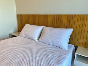 Un lit recouvert d’une courtepointe blanche, avec deux oreillers et une tête de lit en bois.