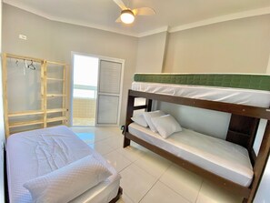 A bunk bed with a green headboard, a wooden wardrobe, and a sliding glass door leading to a balcony. - Edifício Breno Navarro  (Praia Grande)